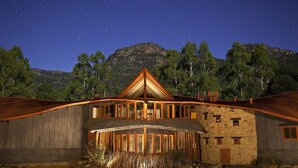 Una cabaña rústica con un techo triangular llamativo, amplias ventanas y fachada de piedra, ubicada frente a un paisaje montañoso.