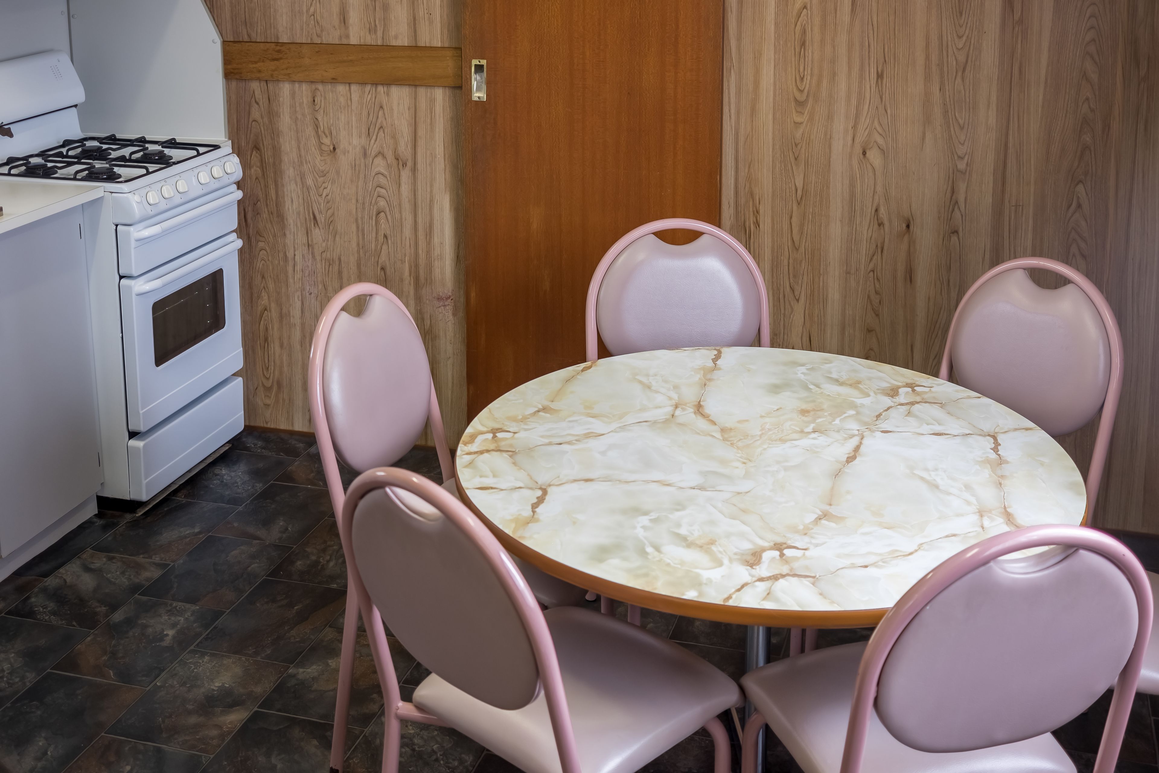 A kitchen with a white stove, a round marble table, and four pink chairs.