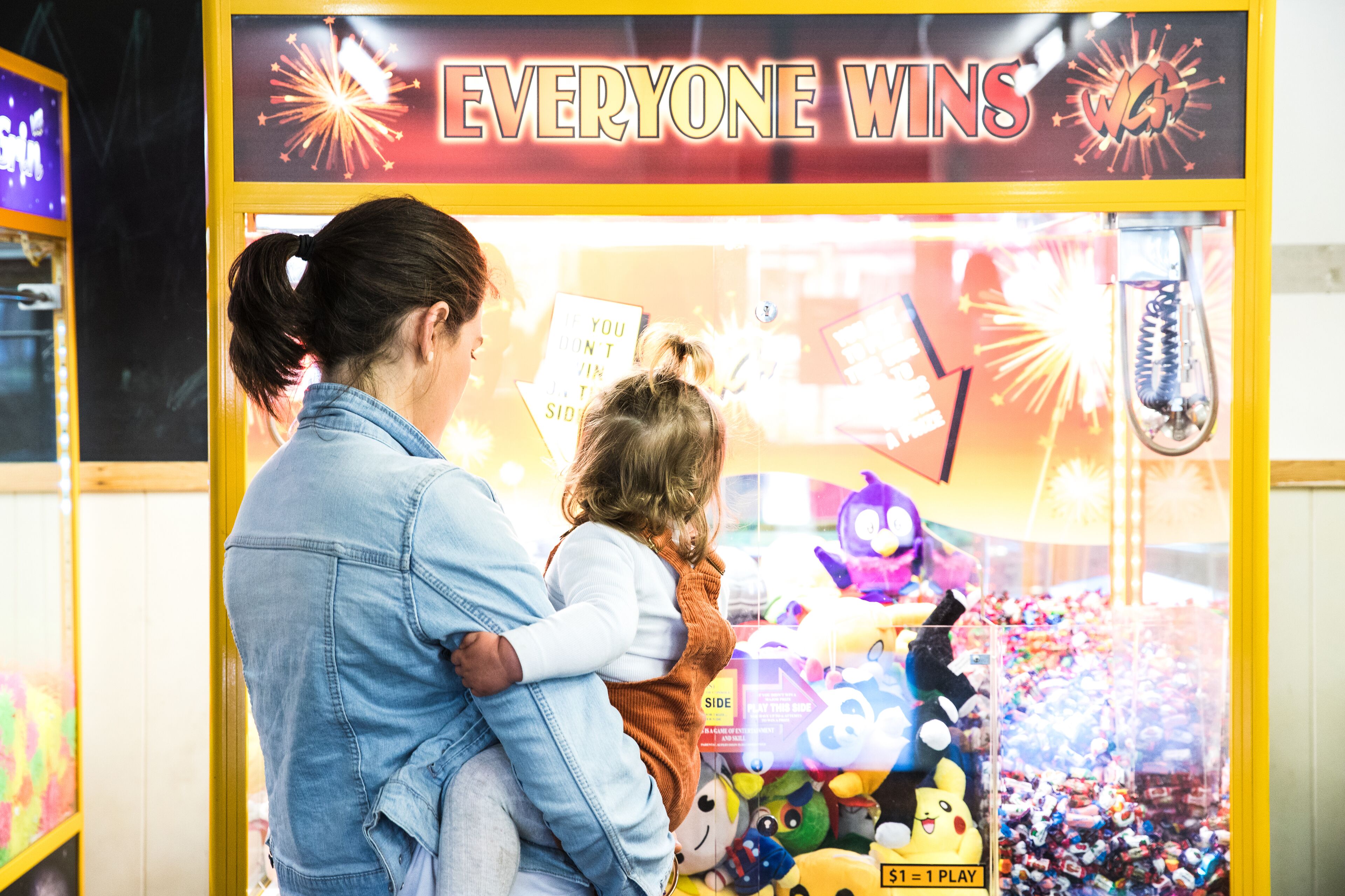 A claw machine with the sign "EVERYONE WINS" and a child holding a sign that says "IF YOU DON'T WIN, YOU'RE A WINNER".