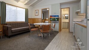 Una sala de estar moderna con sofá, mesa de comedor y sillas, un área de cocina con armarios y electrodomésticos, y un ventanal con cortinas.