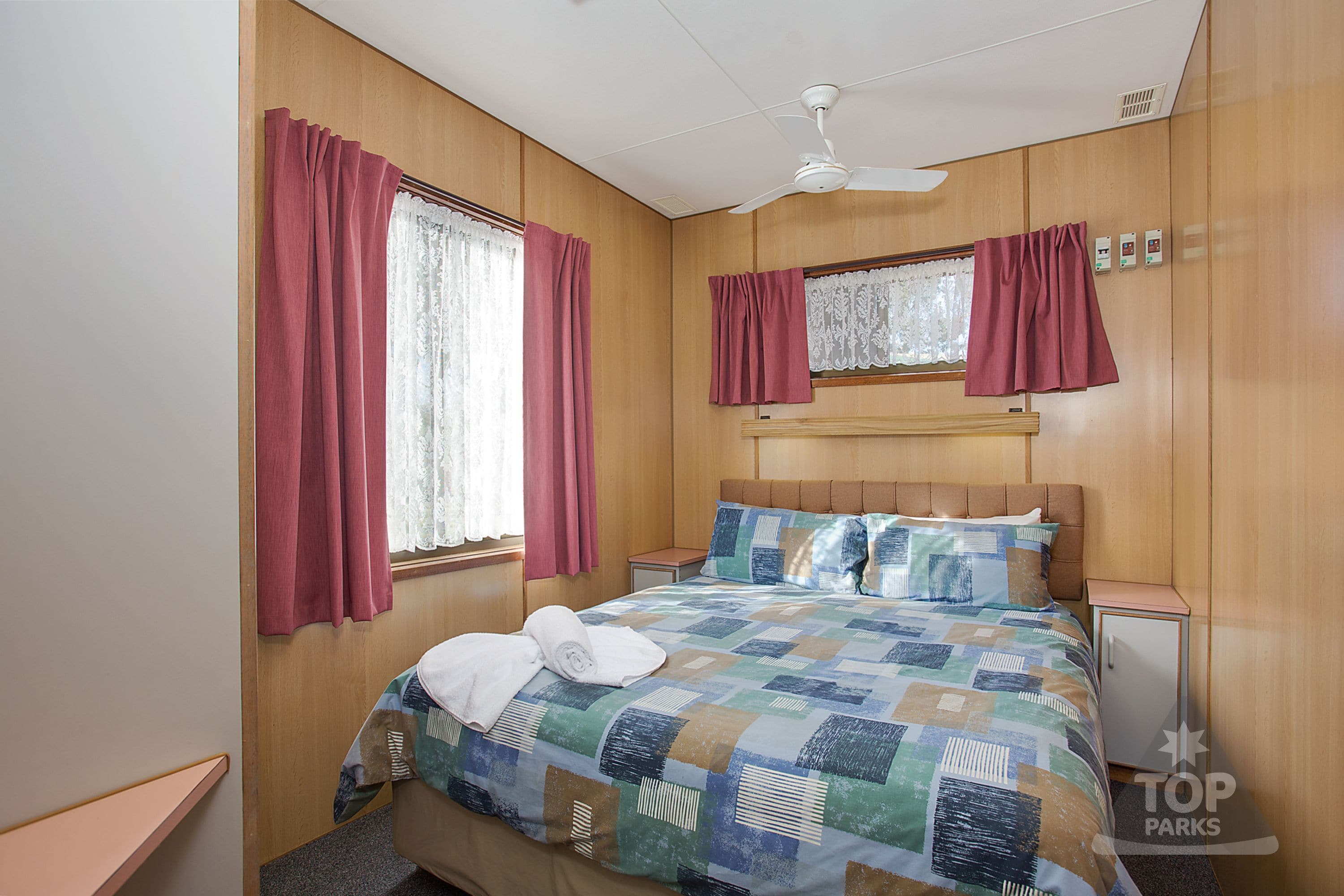 Une chambre à coucher avec une tête de lit en bois, une couvre-lit matelassée, un ventilateur de plafond et une fenêtre avec des rideaux.