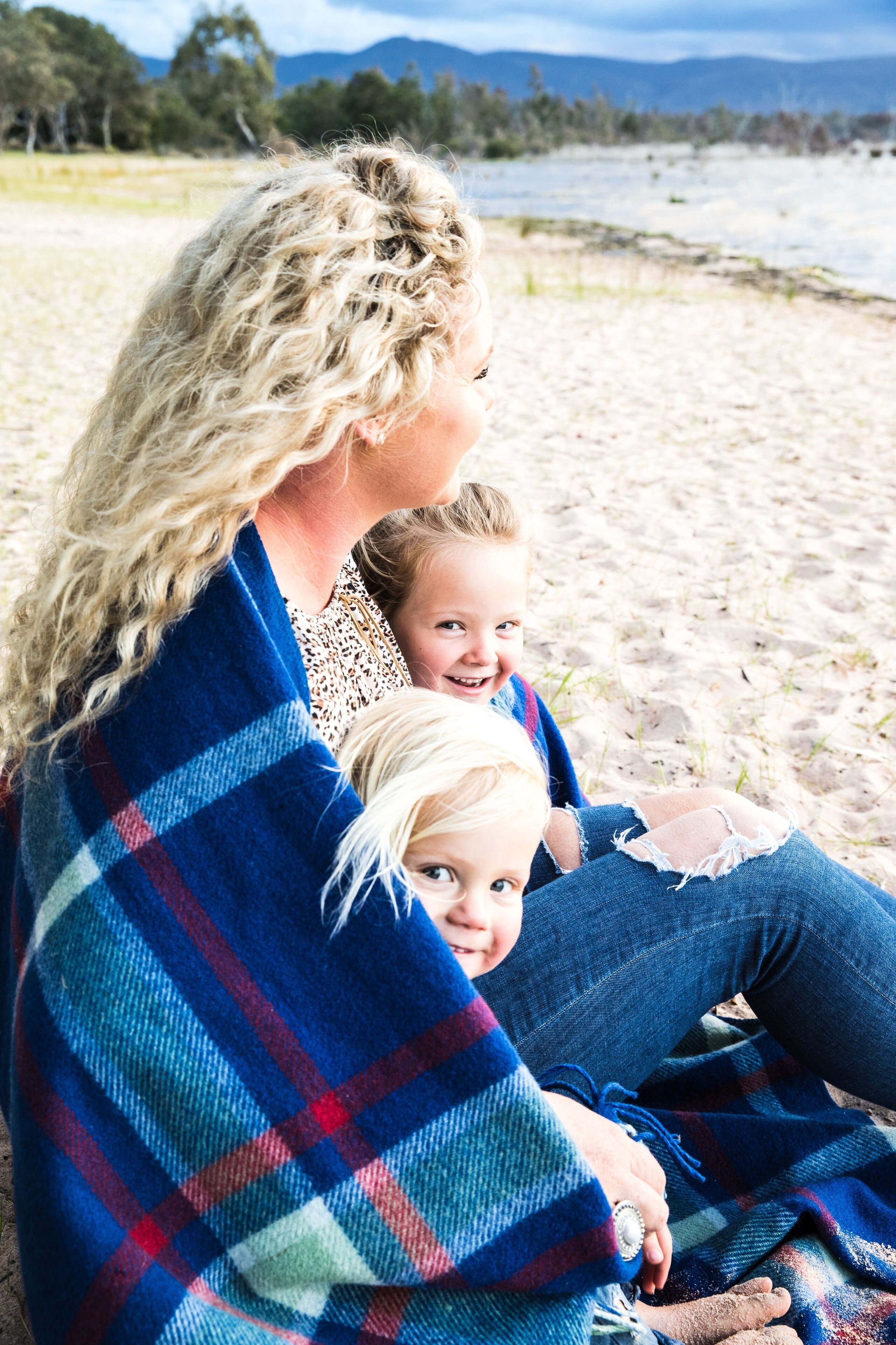 A person sitting on a sandy beach with a blue and red plaid blanket.