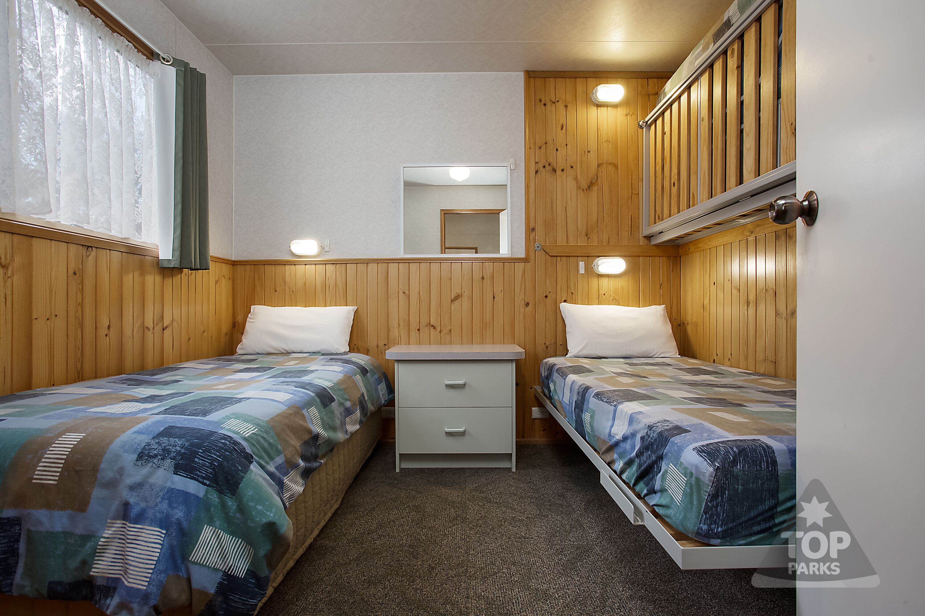 Une chambre avec deux lits, une table de chevet, un miroir et un lambris en bois.