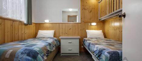 Une chambre avec deux lits, une table de chevet, un miroir et un lambris en bois.