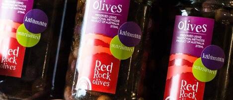 Three jars of Red Rock olives, preserved using traditional methods, held by a person.