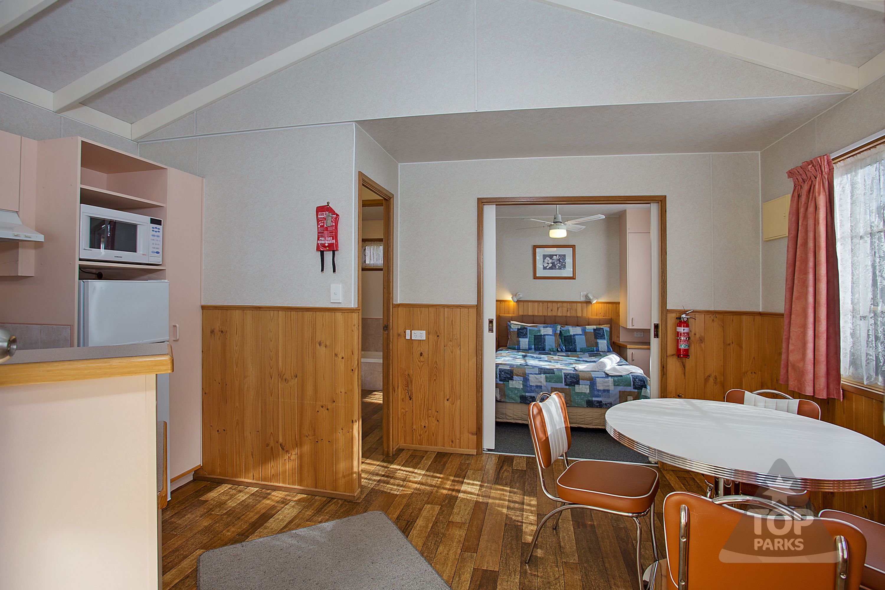 A compact room with a bed, kitchenette, and a dining area with a table and chairs.