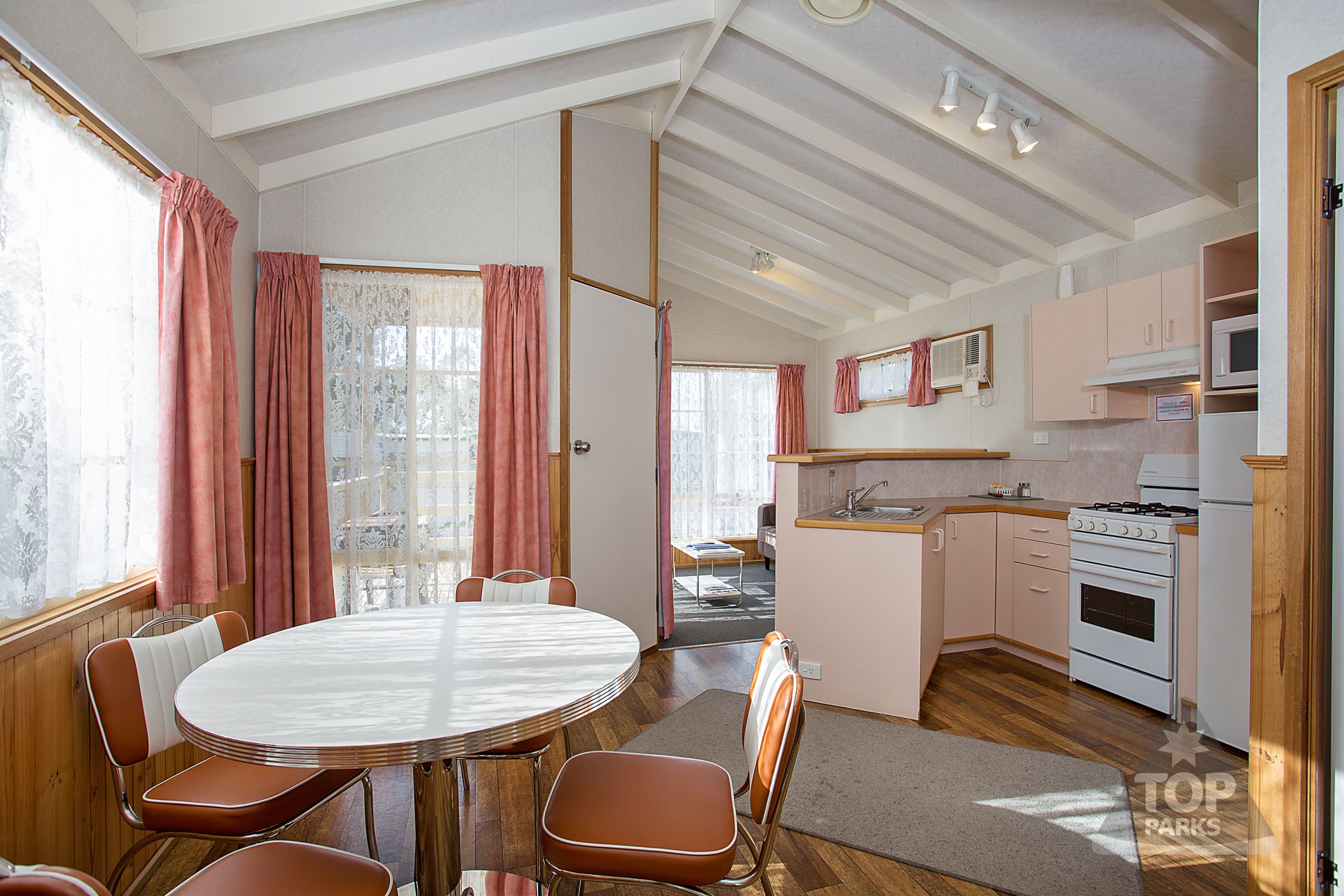 Cocina compacta con estufa, microondas y lavamanos. Zona de comedor con una mesa redonda y sillas.