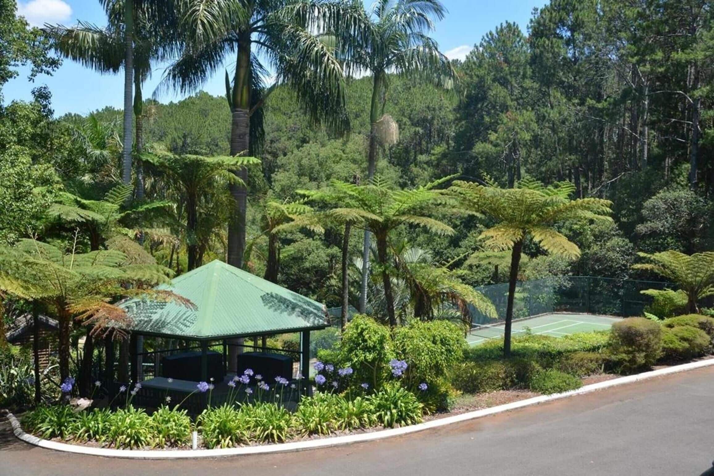 A gazebo surrounded by lush greenery and a tennis court.
