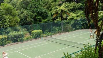 An outdoor tennis court surrounded by dense greenery.