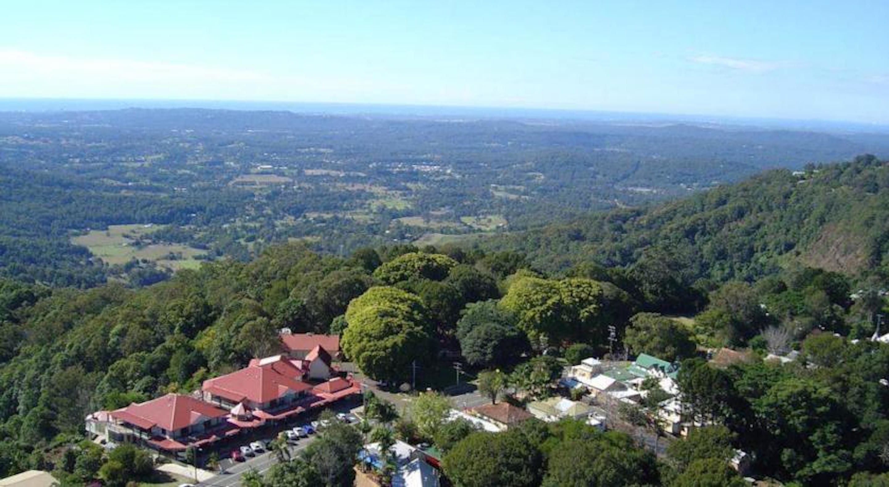 A large building with a red roof surrounded by dense forest and a view of a valley.