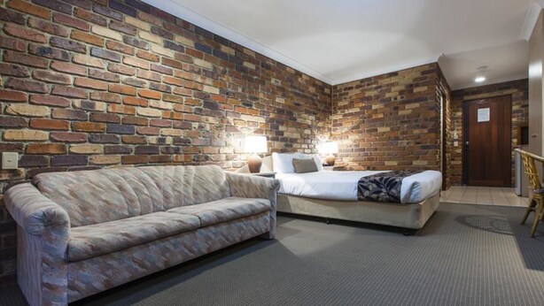 A hotel room with a brick wall, a sofa, a bed, and a wooden door.