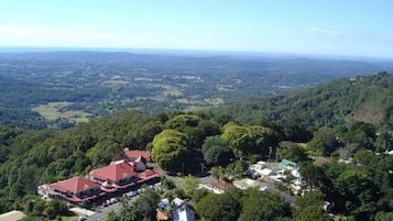 An aerial view of a residential area with houses surrounded by dense forest, a main road, and a clear sky.