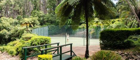 Cancha de tenis rodeada de abundante vegetación y una terraza de madera.