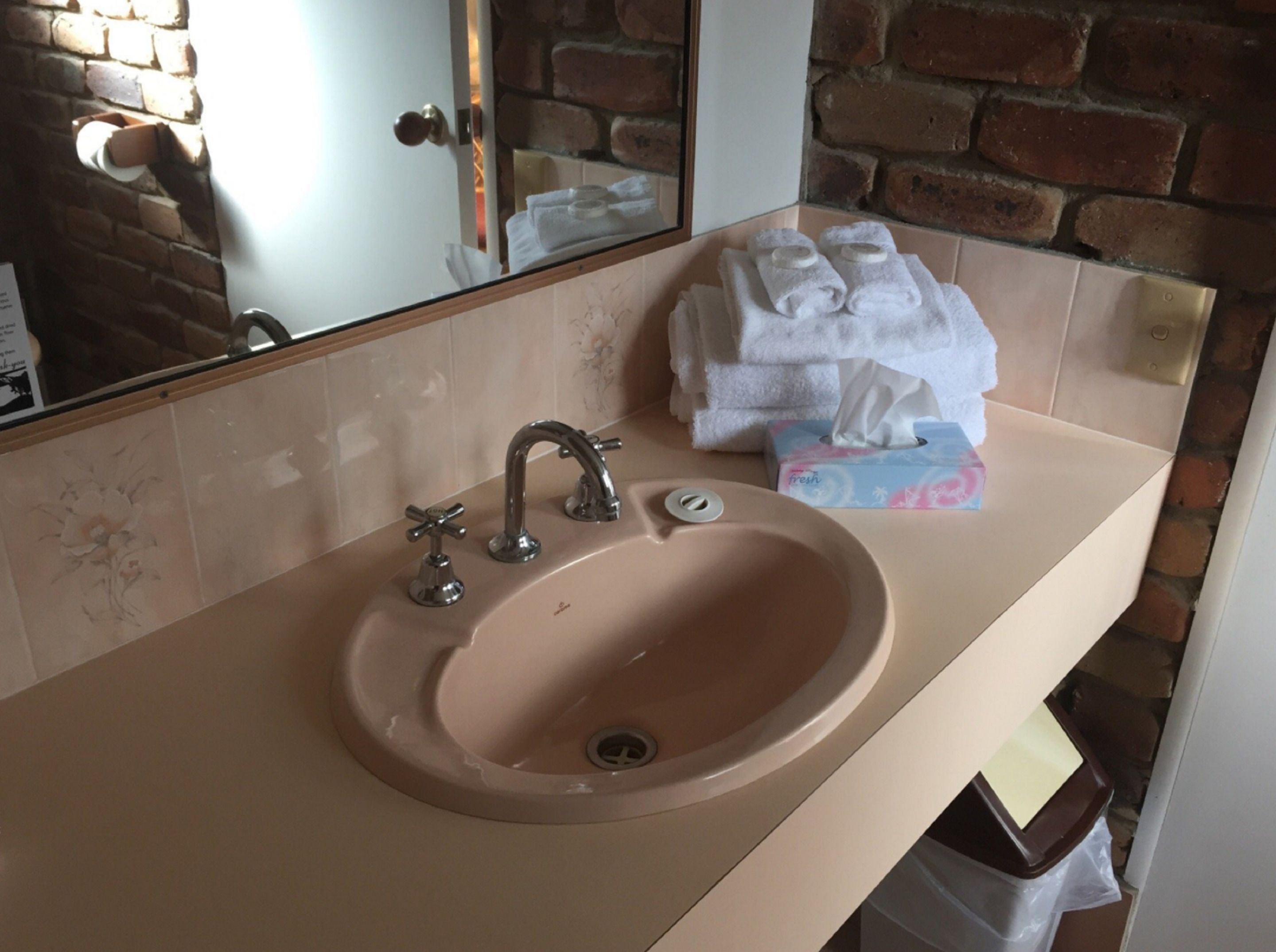 Een badkamer met een beige wastafel, een spiegel en een stapel witte handdoeken.