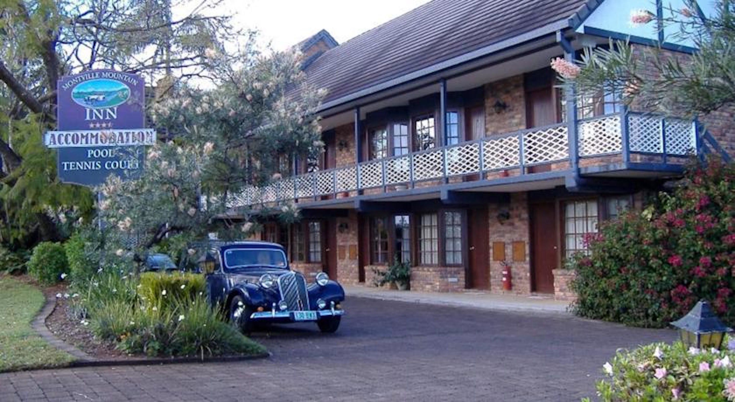 Un hôtel de montagne à Montville, avec une façade en briques, un balcon et une voiture ancienne garée devant.