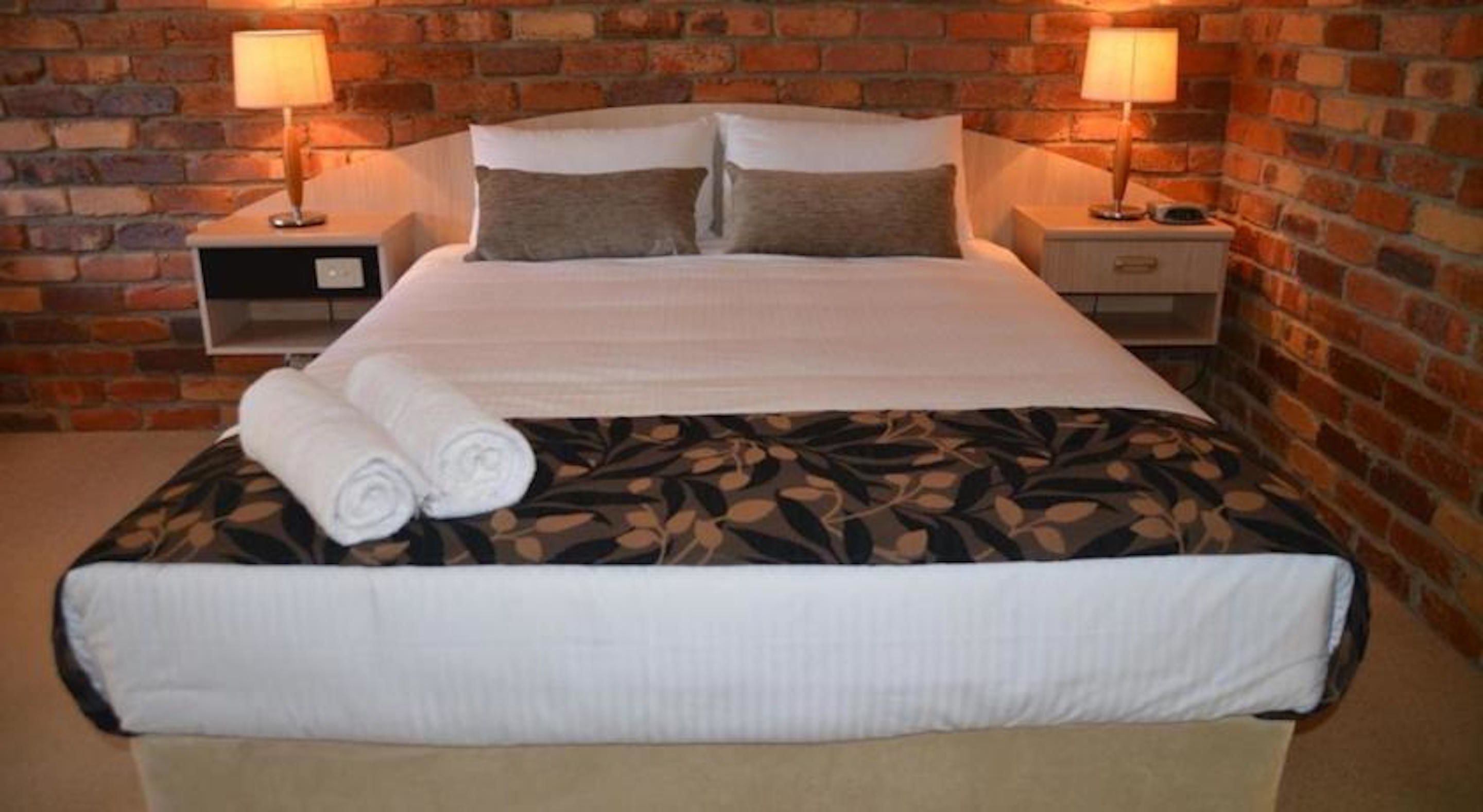 A neatly made bed with a floral bedspread, two pillows, and rolled towels on the side.