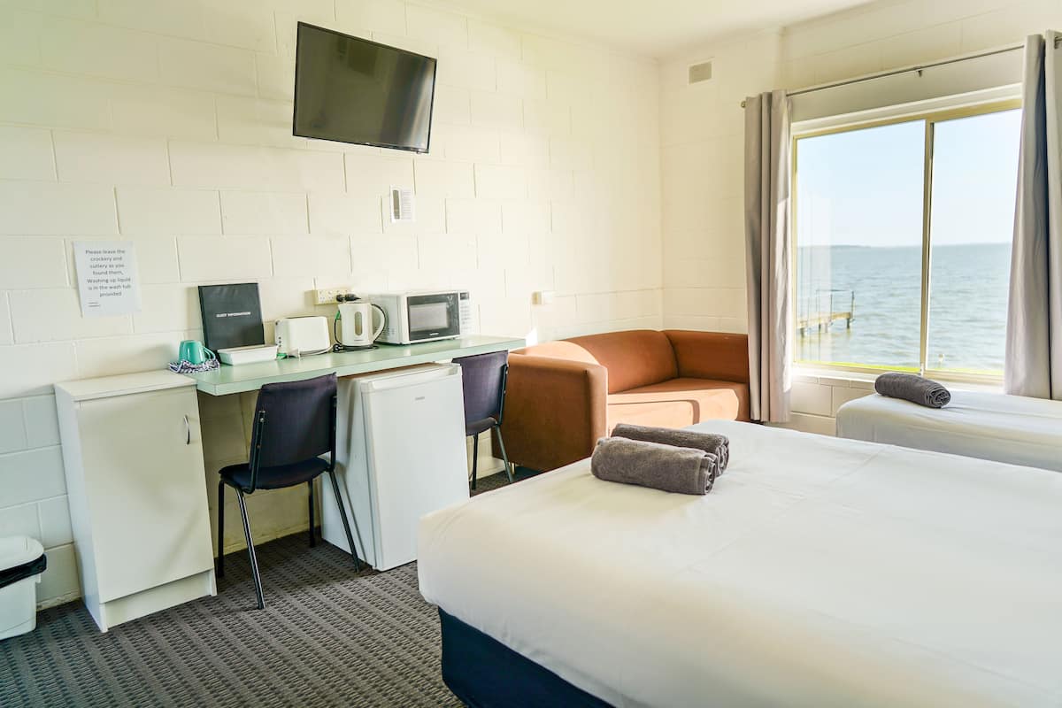 Habitación de hotel con cama, escritorio con computadora y microondas, una silla y vista al mar a través de una ventana.