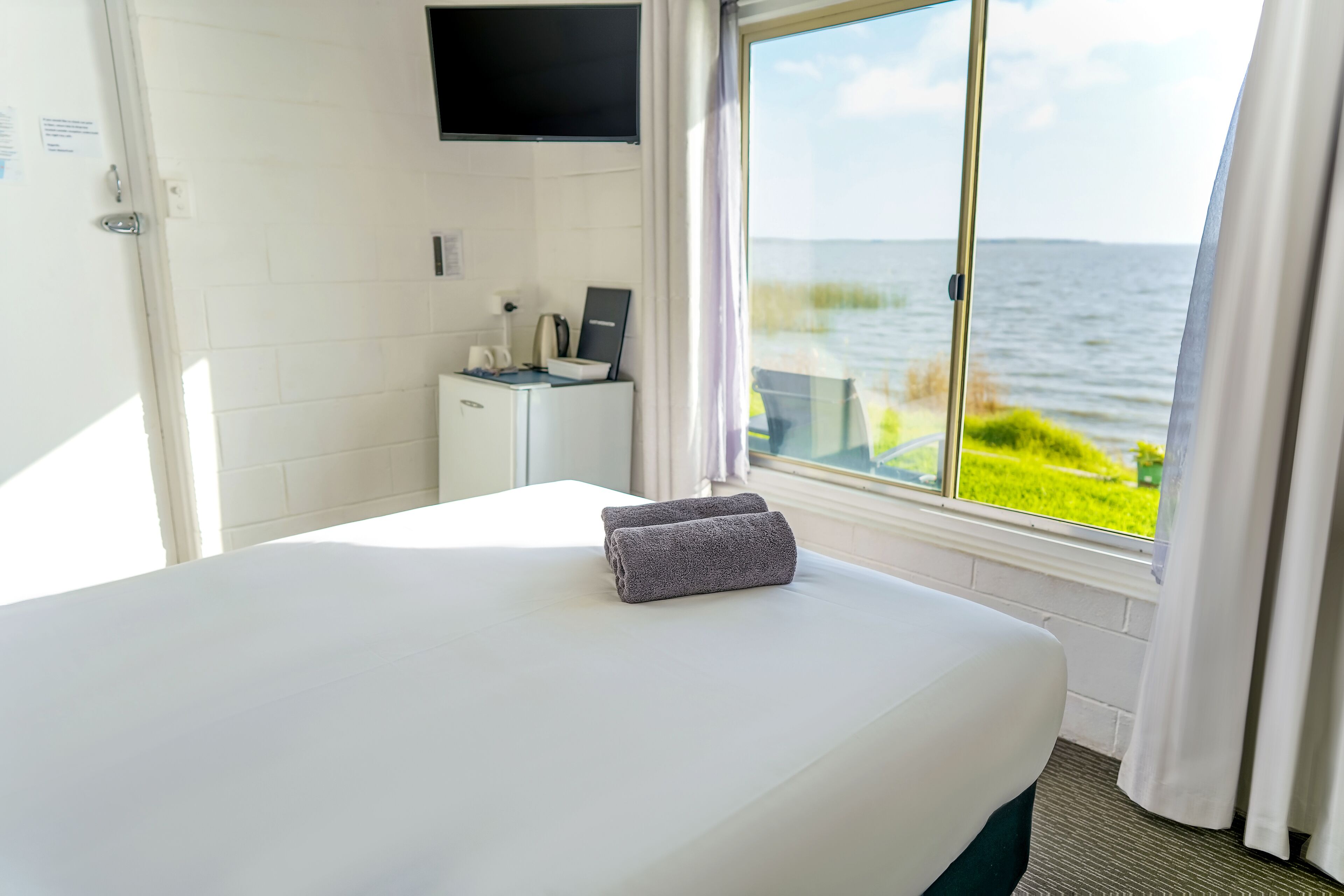 A hotel room with a bed, a desk with a computer, a TV, and a window with a view of the sea.