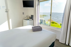 A hotel room with a bed, a desk with a computer, a TV, and a window with a view of the sea. - Meningie's Waterfront Motel (Meningie)