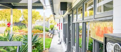 A covered walkway with a bench, potted plants, and a surveillance camera sign.
