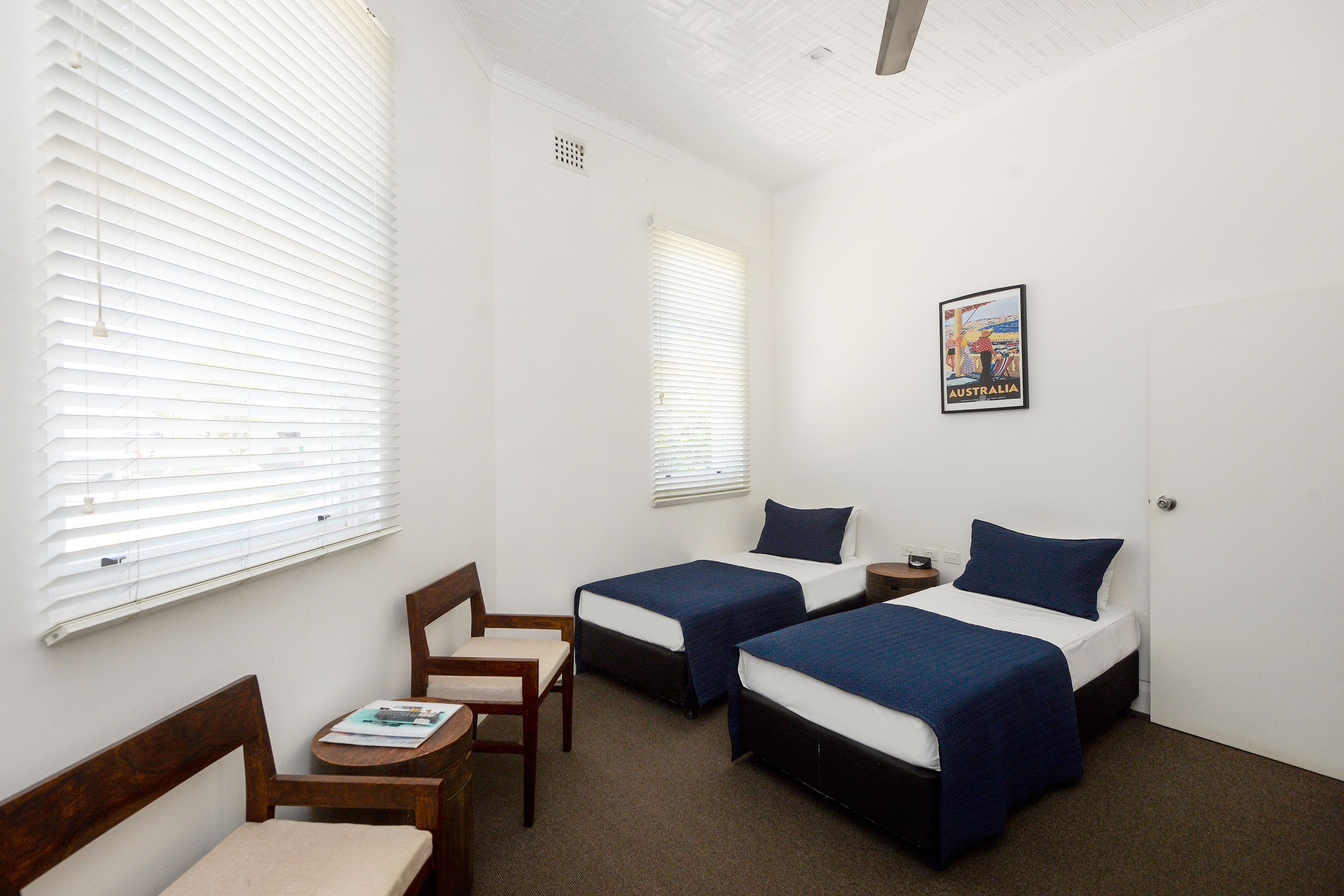 A room with two beds, a chair, a small table, and a poster on the wall.
