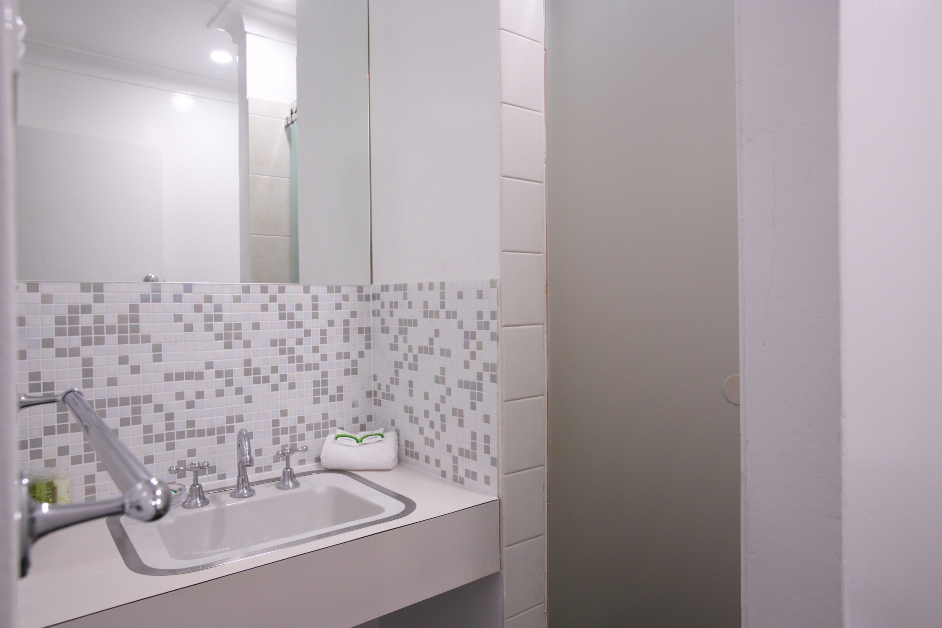 A bathroom with a white sink, multiple faucets, and a tiled backsplash.