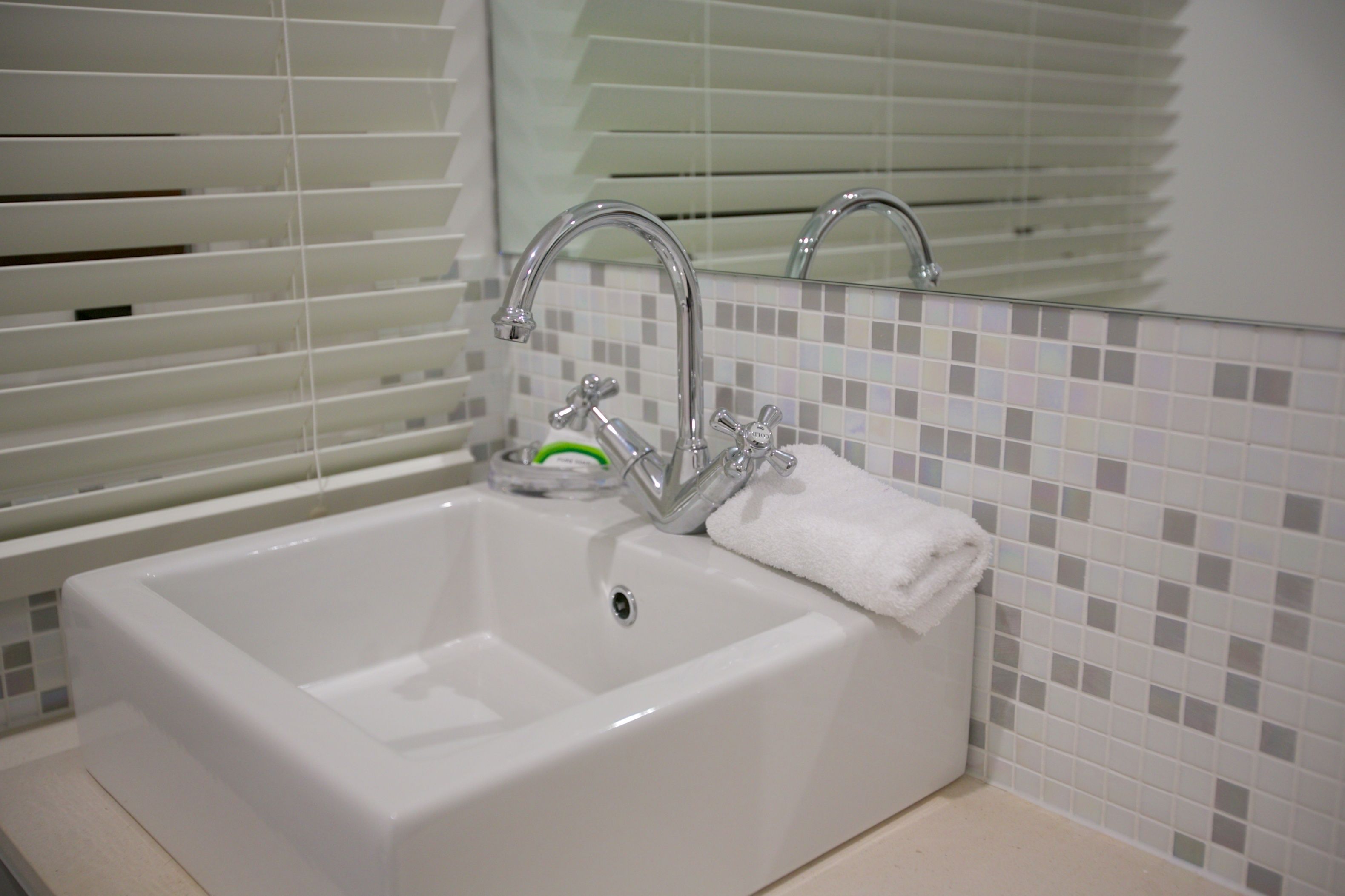 A bathroom with a white sink, chrome faucet, and a mirror above it.