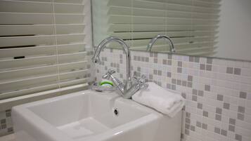 Un baño con lavamanos blanco, grifo cromado y espejo encima.
