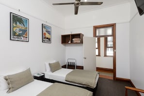 Un dormitorio con dos camas, un ventilador de techo, un estante con artículos de aseo y una puerta que da a otra habitación.