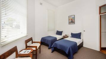 A hotel room with two beds, a small table, and a chair.