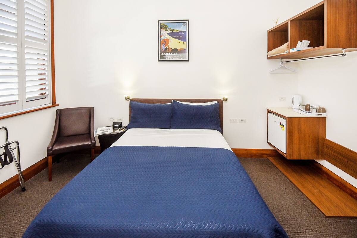 A hotel room with a large bed, a chair, a desk with a computer, and a wooden cabinet.