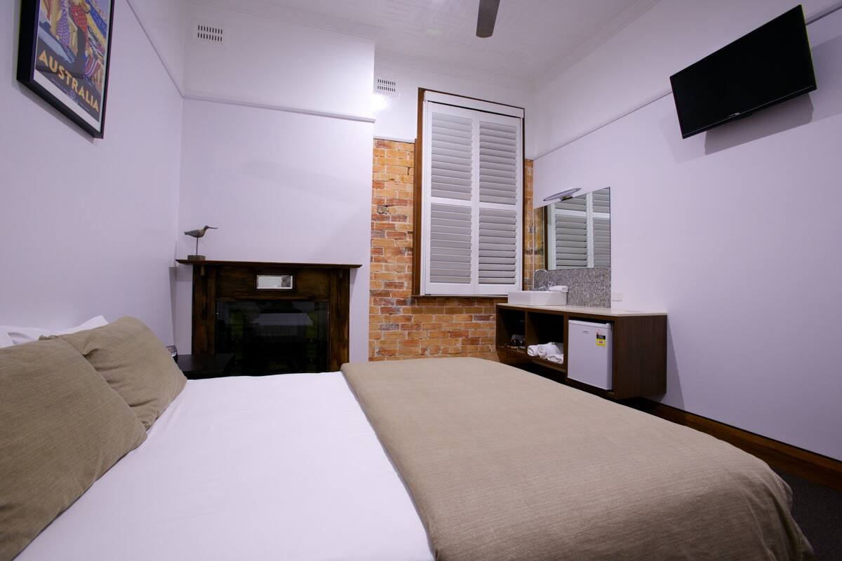 A hotel room with a bed, a small desk, a television, and a brick wall.