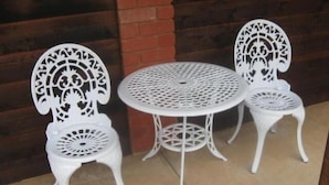 Three white metal chairs with intricate cut-out designs and a round table with a similar pattern, set against a wooden wall. - Country Roads Motor Inn Narrandera (Narrandera)