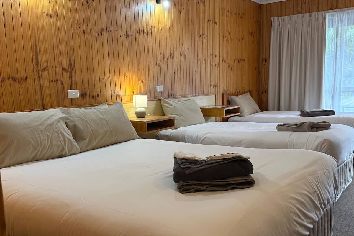Habitació d'hotel amb dos llits, parets de fusta, una taula de nit amb una làmpada i una finestra amb cortines.