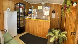 A reception area with a wooden wall, a refrigerator, a glass display case, and a potted plant. - Country Roads Motor Inn Narrandera (Narrandera)