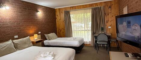 Habitación de hotel con dos camas, un escritorio, un televisor y una ventana con cortinas.