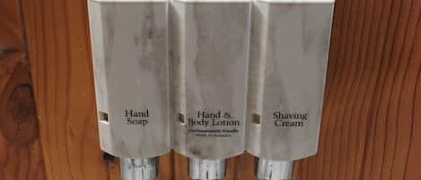 Un distributeur de savon pour les mains, un distributeur de lotion pour les mains et le corps, et un distributeur de mousse à raser, le tout fixé sur une surface en bois.