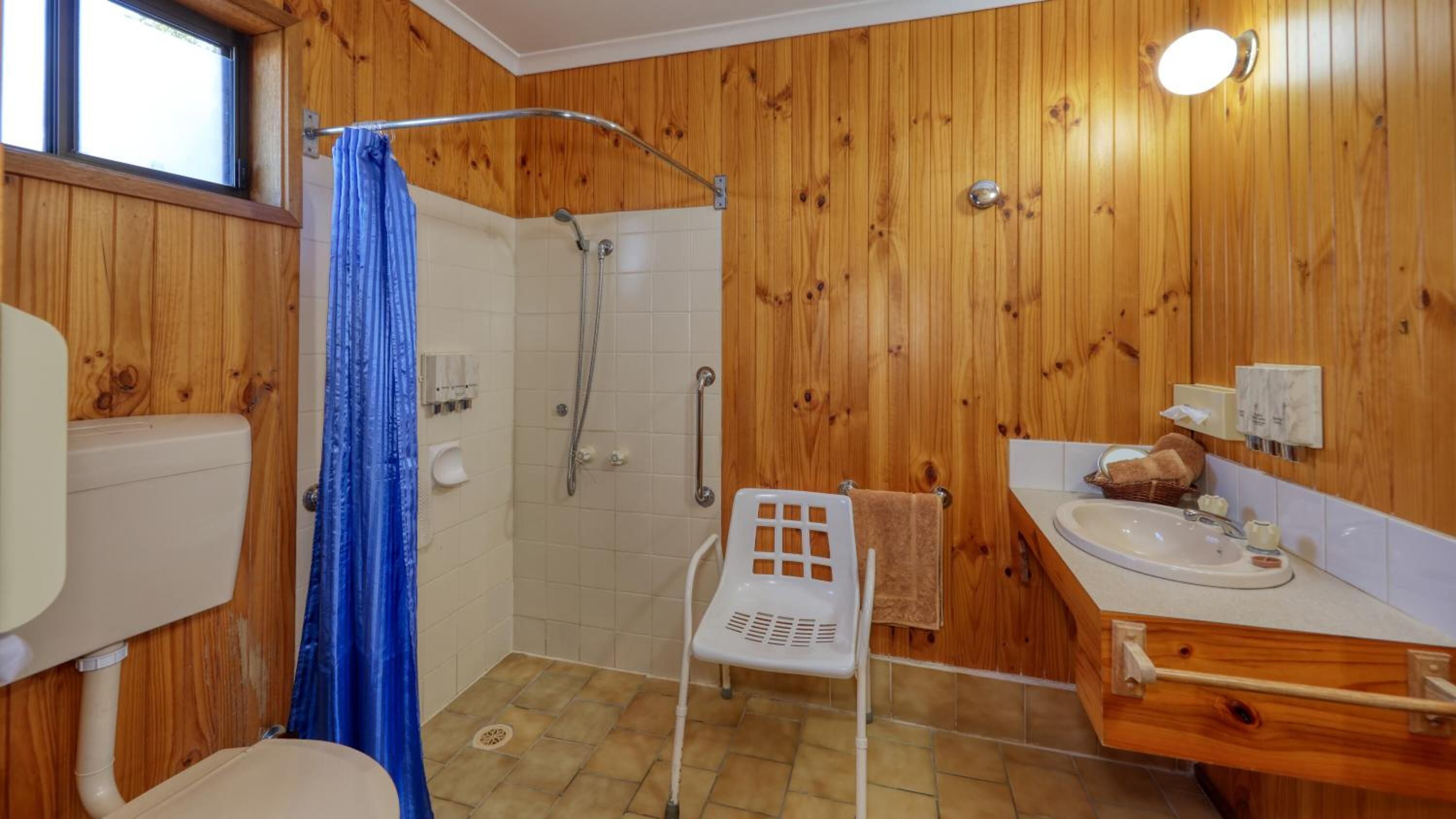 A wooden-paneled bathroom with a shower, toilet, and sink.