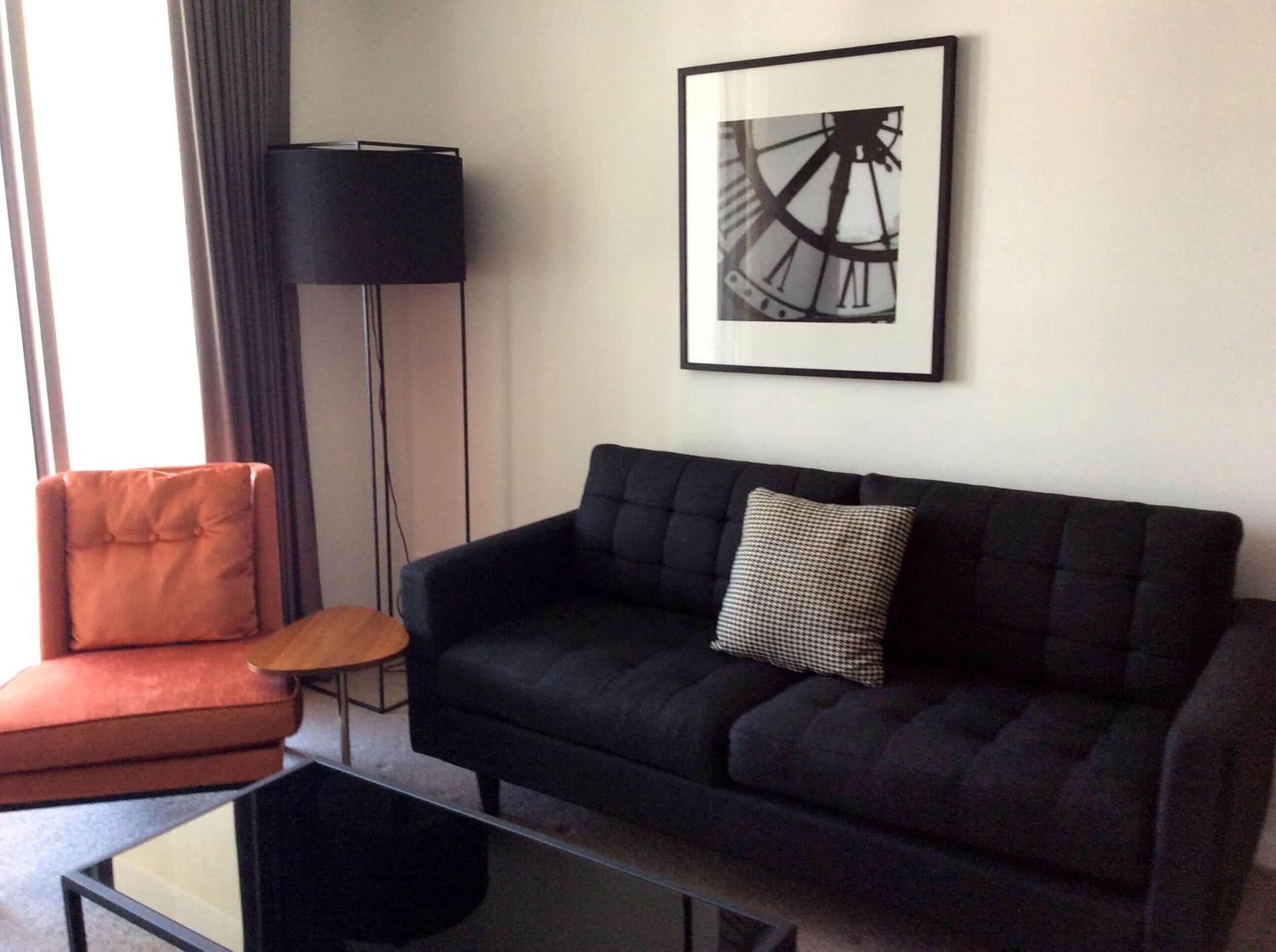 Un salon avec un canapé noir, un fauteuil rouge, une petite table en bois et un lampadaire noir.