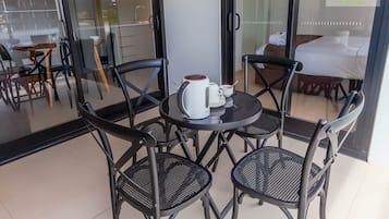 Ett hotellrum med en glasdörr, ett litet runt bord med en vattenkokare och koppar, och en säng med ett vitt överkast.