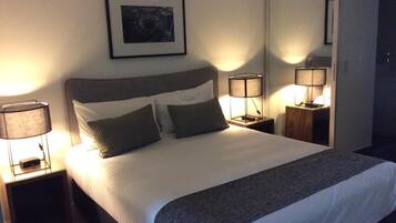 Un letto rifatto con cura, con una testiera grigia, due lampade ai comodini e un quadro incorniciato appeso al muro.
