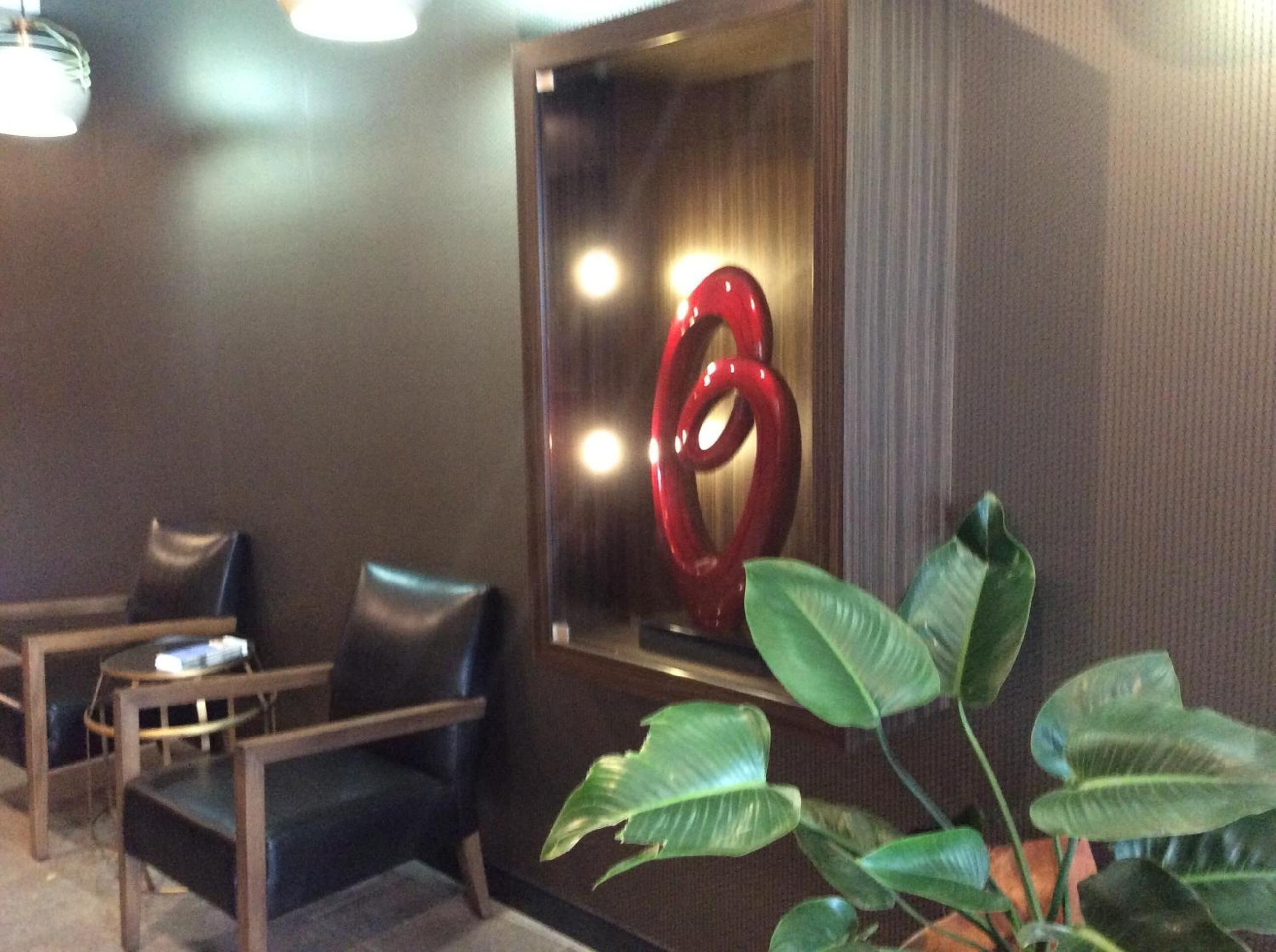 A room with a large red sculpture, a plant, and two leather chairs.
