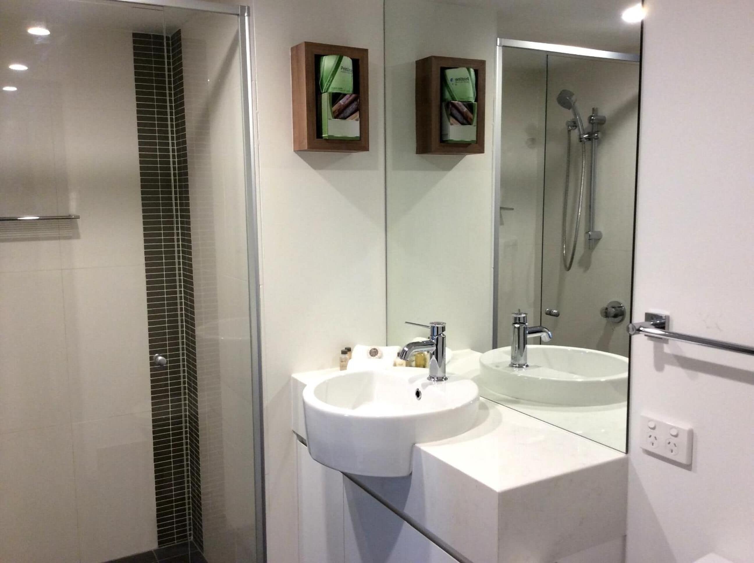 A modern bathroom with a glass shower enclosure, two sinks, and a large mirror.