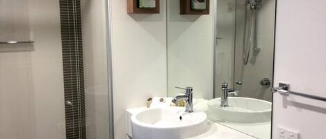 A modern bathroom with a glass shower enclosure, two sinks, and a large mirror.