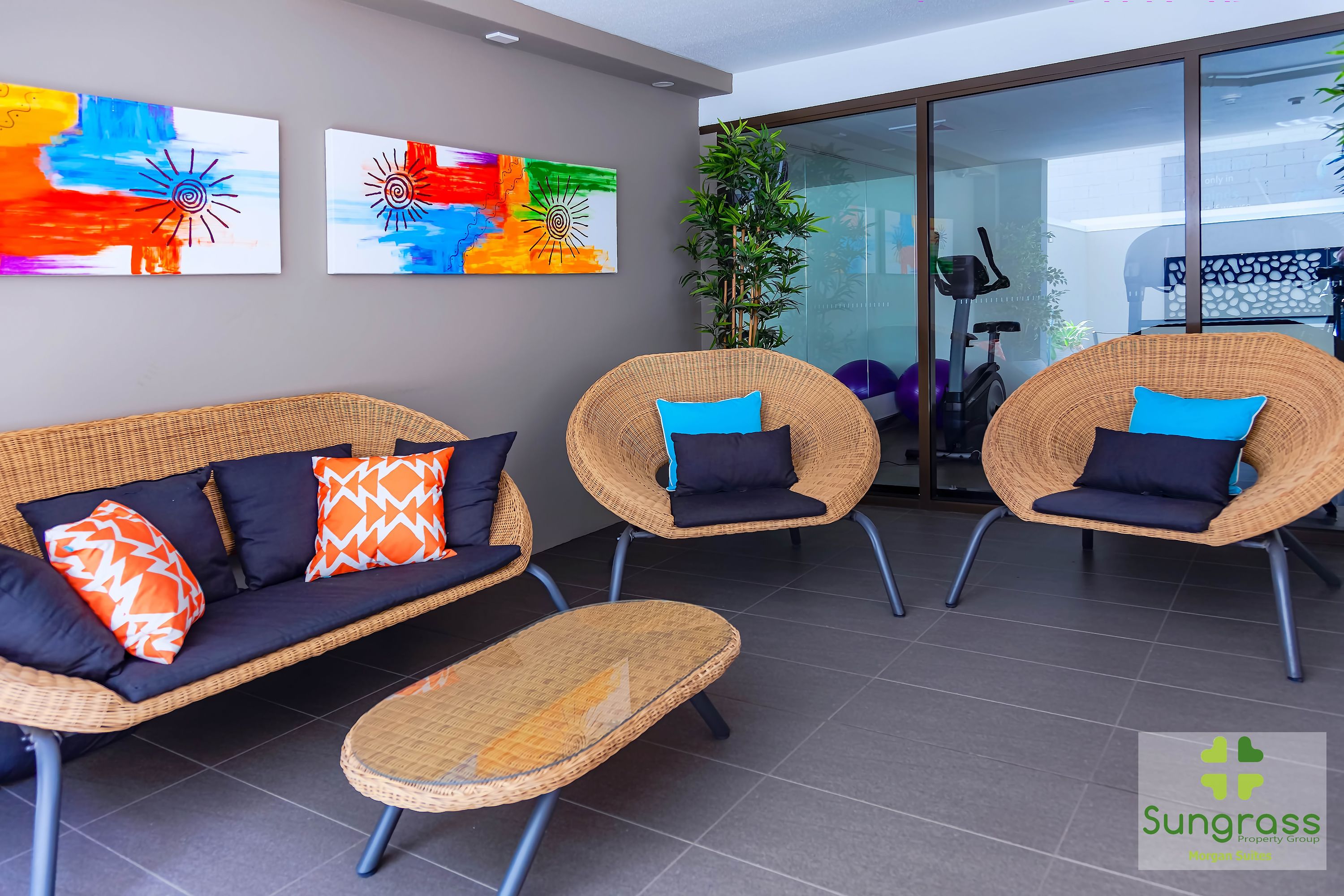 Un espace d’attente moderne, doté de meubles en osier, d’un canapé avec des coussins à motifs et d’œuvres d’art abstraites accrochées aux murs.
