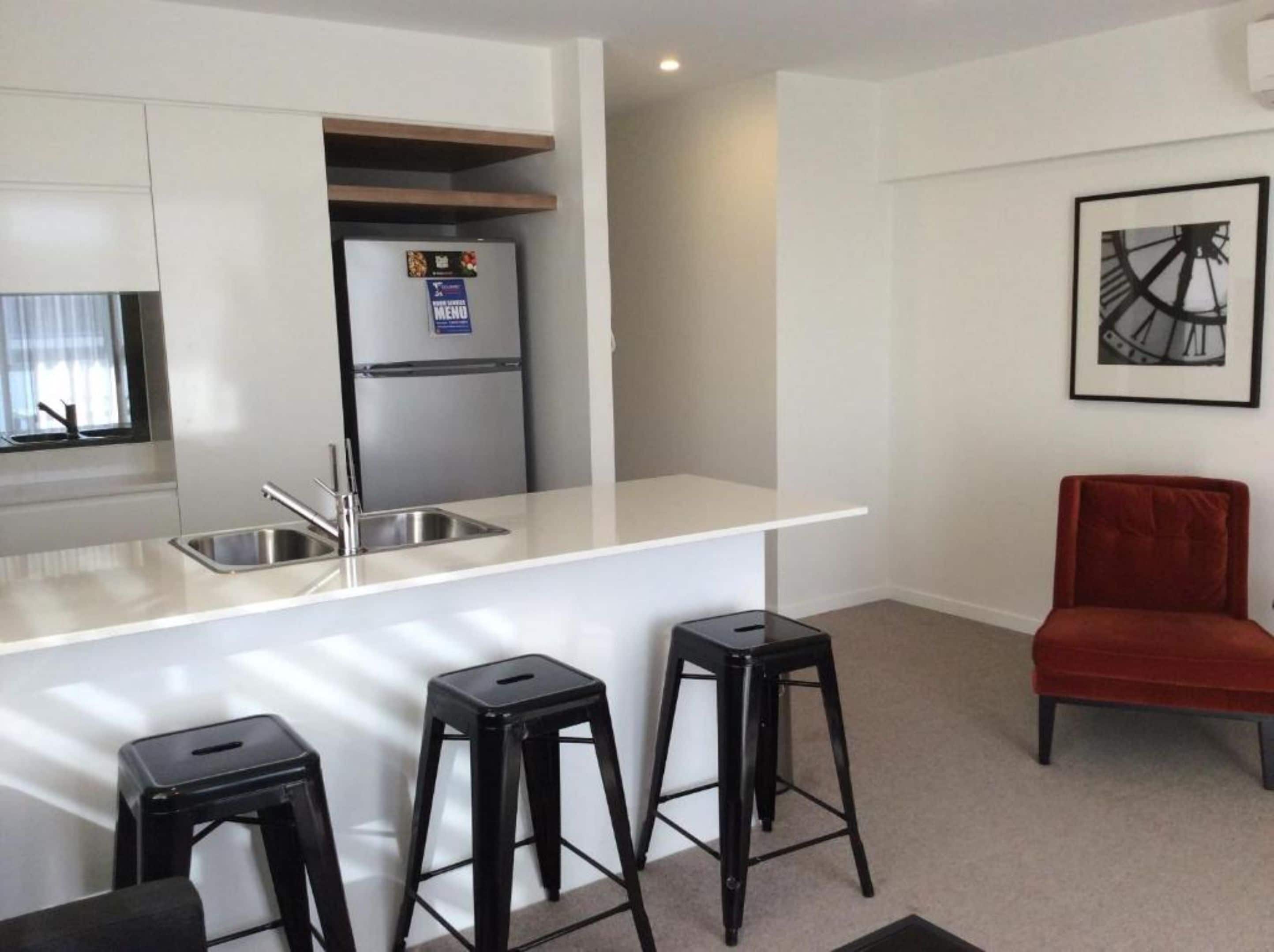 A modern kitchen with a stainless steel refrigerator, a white countertop, and a bar stool.