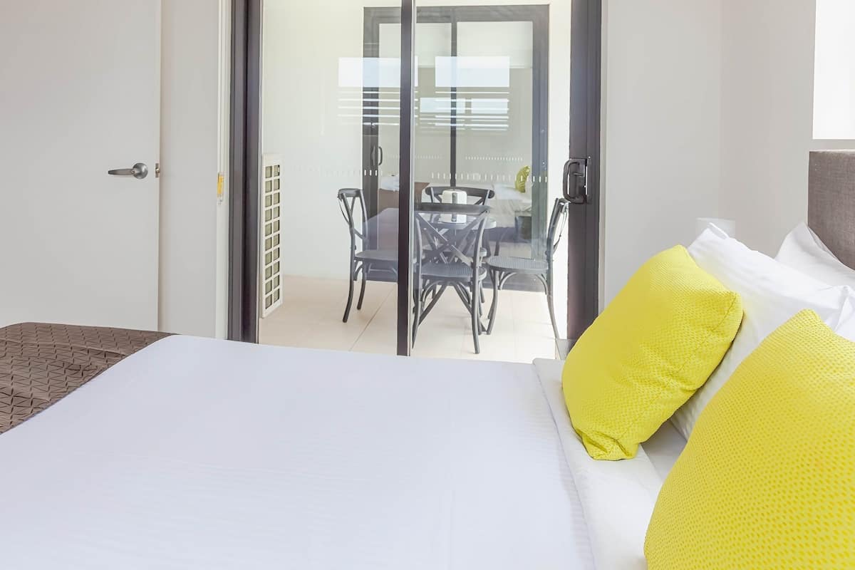A hotel room with a bed, a desk, and a view of a balcony with a table and chairs.