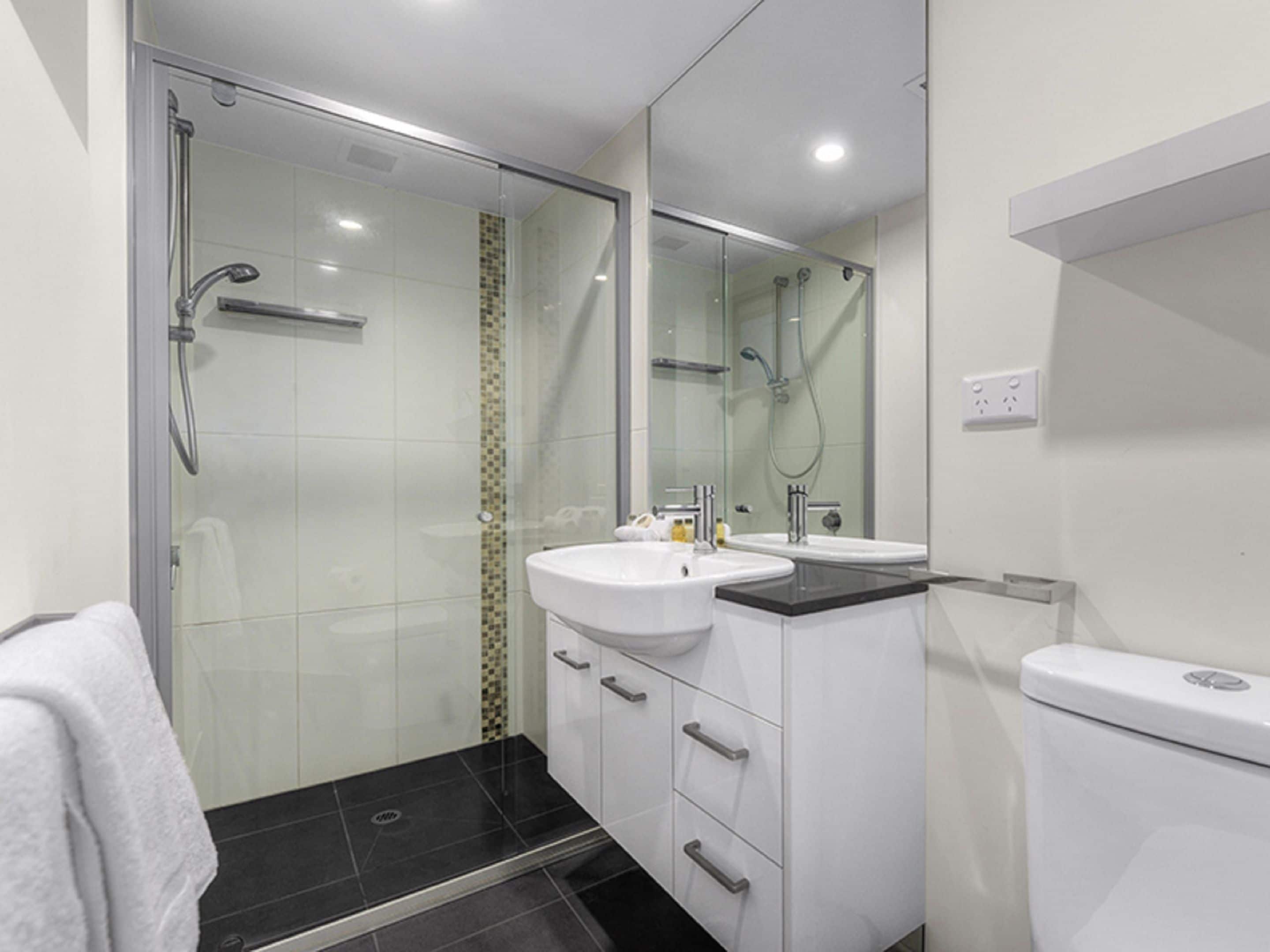 A modern bathroom with a glass shower enclosure, a white sink, and a toilet.