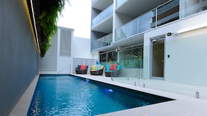 Une piscine intérieure moderne, avec une eau d’un bleu cristallin, entourée d’une terrasse carrelée de blanc et de rampes de protection en verre.