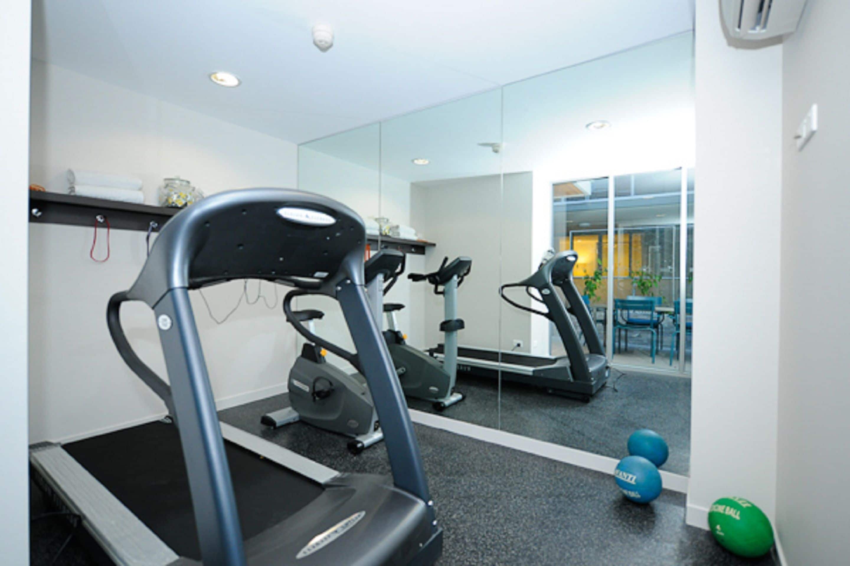 Une salle de sport équipée de tapis de course, de ballons d’exercice et d’un miroir qui reflète l’ensemble de la pièce.